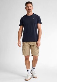 Merimiesten pyöreäkauluksinen t-paita yhdistettynä beigenvärisiin cargo-shortseihin. Sukat, joissa on kaksi mustaa viivaa, ja valkoiset tennarit täydentävät asun.