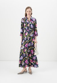Floral long dress with button front, navy background, pink and blue flowers, three-quarter sleeves. Paired with cream handbag and gray heels.