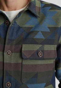 Camicia con bottoni caratterizzata da un motivo geometrico in teal, verde e marrone. Tessuto testurizzato con due tasche sul petto e bottoni a contrasto.