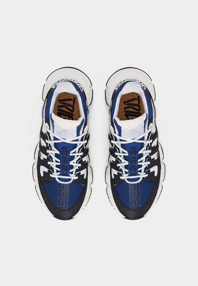 Ζευγάρι αθλητικών παπουτσιών Versace σε μπλε, μαύρο και λευκό χρώμα, με κορδόνια και έντονα λογότυπα, απεικονιζόμενο από πάνω σε λευκό φόντο.