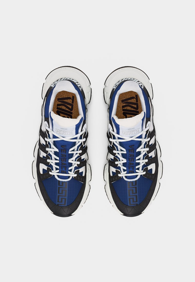Paire de baskets Versace bleu, noir et blanc avec lacets et motifs de logo audacieux, vues de dessus sur un fond blanc.