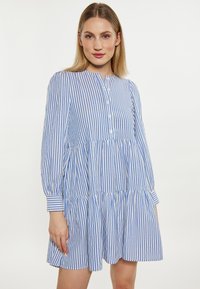 Abito a righe blu e bianche con design a strati, maniche lunghe, chiusura con bottoni e scollatura rotonda. Tessuto leggero con una vestibilità morbida.