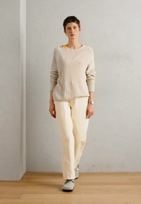 Jasno beżowy sweter w prążki, luźny krój. Off-white spodnie w prostym kroju z subtelnym przeszyciem. Jasnoszare buty. Minimalistyczny design na szarym tle.