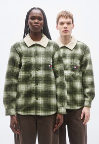 Geruite overhemden in groene tinten met licht beige sherpa-kragen. Elk beschikt over twee borstzakken en een merklogo-patch aan de linkerkant.