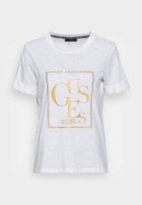 Bílý bavlněný tričko s zlatým grafickým potiskem se texty "LOS ANGELES" a "GUESS". Klasický design s kulatým výstřihem a ohrnutými rukávy.