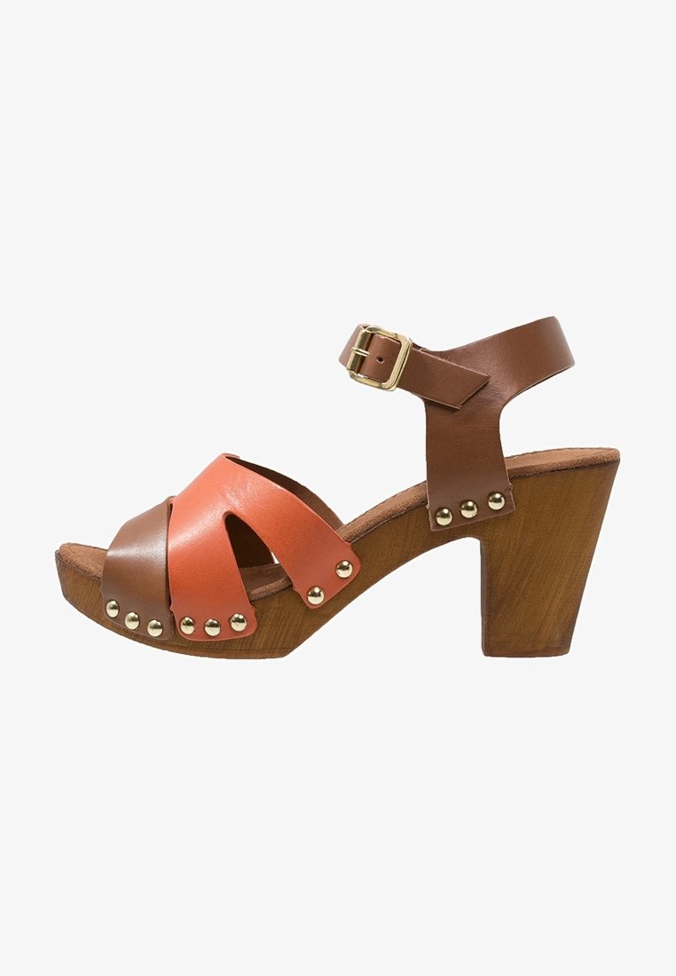 Sandale ouverte en cuir marron et orange avec talon carré en bois, bride à la cheville, boucle dorée et accents en clous métalliques.