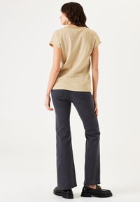 Top beige de manga corta con escote redondo combinado con jeans acampanados gris oscuro y mocasines de plataforma negros. Tela texturizada visible.