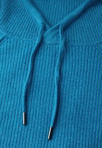Haut à capuche bleu texturé avec un design en V, fabriqué en maille côtelée, et cordons contrastés avec des embouts métalliques.