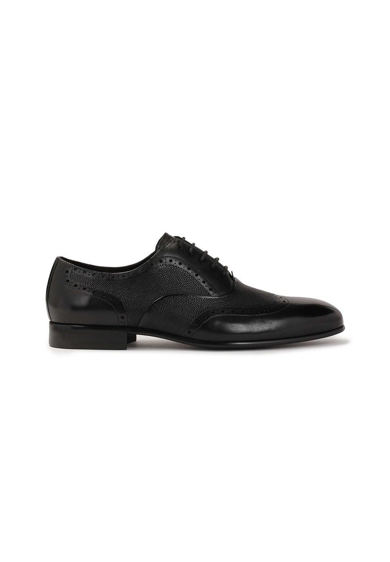 Chaussure habillée en cuir noir avec un capuchon de orteil lisse et des détails de brogue, présentant un panneau latéral texturé et un talon plat.