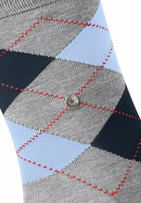 Strikkede argyle-sokker med grå, navy og lyseblå diamanter, rød syning og et metallisk logo-detalje. Tekstureret stofkomposition.