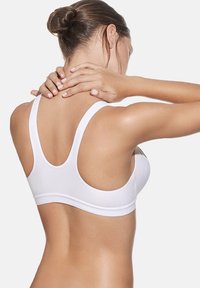 Sostén deportivo blanco con tirantes anchos y una textura suave. Diseñado con un estilo de espalda de nadador, presenta una silueta minimalista y una banda elástica.