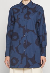 Chemise à manches longues en coton bleu foncé, ornée de grands motifs floraux bleu marine, boutonnière à l'avant et col pointu. Texture lisse avec une coupe standard.
