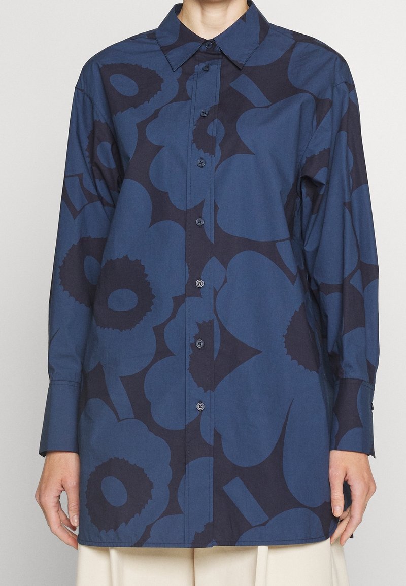 Chemise à manches longues en coton bleu foncé, ornée de grands motifs floraux bleu marine, boutonnière à l'avant et col pointu. Texture lisse avec une coupe standard.