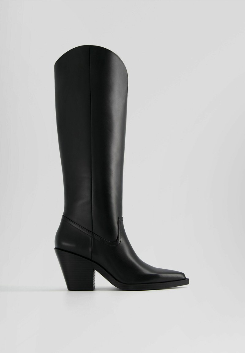 Bottes noires en cuir montantes avec un bout pointu et un talon carré. Texture lisse avec une couture minimale et un bord supérieur arrondi.