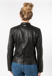 Schwarze Lederjacke mit strukturierten Schultern, klaren Nähten und einem taillierten Schnitt. Mit rundem Kragen und zentralem Druckknopfverschluss auf der Rückseite.