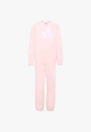 Zestaw jasnoróżowej bluzy i spodni dresowych z białym logo Adidas na piersi i lewej nodze, przedstawiony na białym tle.