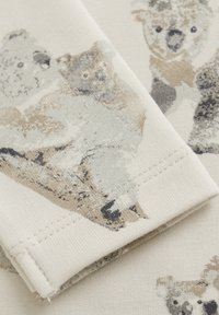 Baumwollstoff mit einer gemusterten Darstellung von Koalas in sanften Beige- und Grautönen, mit einer glatten Textur und sichtbaren Nähdetails.