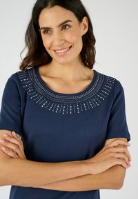 T-shirt in cotone blu navy con scollatura rotonda, decorata con perline argentate e cuciture a motivo a raggiera attorno al colletto.