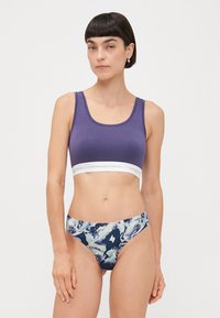 Lilla bomullssportsbh med et hvitt elastisk bånd som har "Copenhagen Studios" logo. Matchende flerfarget marmorert bikinitruse.