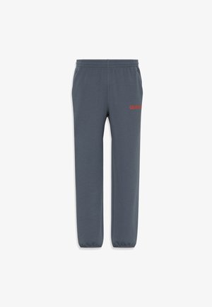 Pantaloni tuta grigi con elastico in vita e alle caviglie, caratterizzati da un tessuto testurizzato e dal logo rosso "CALVIN KLEIN" sulla coscia sinistra.