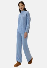 Suéter de punto trenzado azul claro con cuello alto, combinado con pantalones de pierna ancha a juego; textura suave; calzado marrón completa el conjunto.