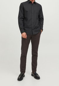 Svart långärmad skjorta med knappar, i bomull, kombinerad med mörkbruna byxor och svarta läderskor. Enkel design, åtsittande stil.