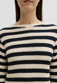 Pull en tricot rayé avec de larges rayures horizontales bleu marine et crème, fabriqué dans un tissu texturé et ample, avec un col rond.