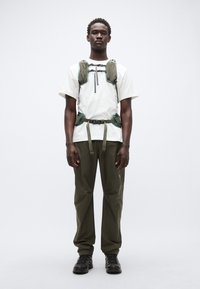 Ελαφρύ, λευκό πουκάμισο με κοντά μανίκια. Πράσινο ζευγάρι με θήκες, μαύρο φερμουάρ, χακί παντελόνια και μαύρα παπούτσια. Μινιμαλιστικό εξωτερικό στυλ.