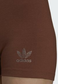 Hnedé bavlnené kraťasy s lesklým kamienkovým logom Adidas na ľavom stehne, so priliehavým strihom a hladkou textúrou.