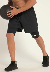Shorts de sport noirs avec une doublure ajustée noire et des lettres blanches sur la jambe gauche. Chaussures de sport noires. Tenant un ballon de basket noir.
