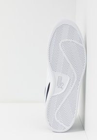 White sneaker sole with a textured rubber pattern and herringbone tread. Features a logo on a side accent. Simple and streamlined design.