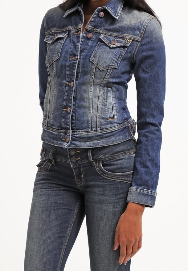 Femme portant une veste en jean bleu ajustée avec fermeture par boutons et un jean en denim bleu assorti avec coutures visibles et braguette à boutons.