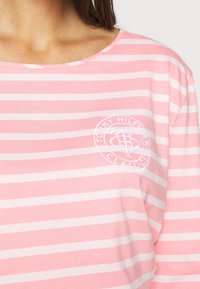 Maglietta a maniche lunghe a righe rosa e bianche, realizzata in morbido cotone, con collo rotondo e un logo circolare ricamato sul petto.