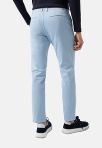 Lichtblauwe chino broek met een rechte snit, voorzien van achterzakken en een soepele katoenen textuur. Gepaard met marineblauwe sneakers.