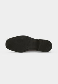 Semelle en caoutchouc noire d'une chaussure habillée pour homme avec un motif de semelle et la marque « GANT » près de la voûte plantaire, présentée sur un fond uni.