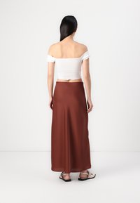 Hvit av-shoulder crop top med ribbet tekstur, sammen med en flytende brun maxi-skjørt laget av glatt stoff, og casual sandaler med stropper.