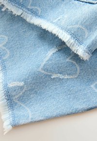Svijetloplavi denim materijal s ispucalim rubovima, s blagim uzorkom srca i teksturiranim tkanjem.
