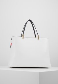 Valkoinen nahkainen olkalaukku mustilla kahvoilla, kultaisilla varusteilla ja värikkäillä sivuainoilla. Sileä pinta ja rakenteellinen muotoilu.