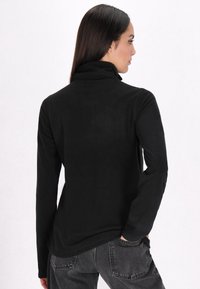 Zwarte, longsleeve, mock-neck shirt van zacht materiaal met een aansluitend ontwerp. Bevat een platte naad en een relaxte silhoeët.