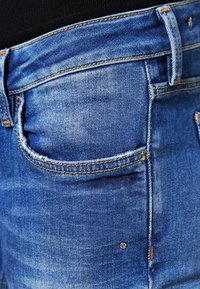 Jeans de mezclilla azul con un diseño clásico de cinco bolsillos, costuras en contraste y una ligera textura desgastada en los bolsillos.