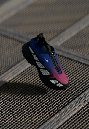 Einzelner Sportschuh mit blau-violettem Farbverlauf am Obermaterial, schwarzer Sohle, weißen Akzenten und Reißverschluss, liegt auf einer strukturierten Metalloberfläche.