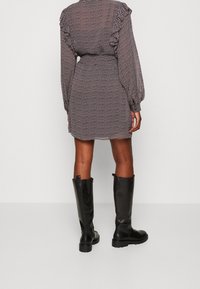 Druckkleid mit voluminösen Ärmel, tailliertem Oberteil und Rückenschnürung; kombiniert mit knielangen, glänzenden schwarzen Stiefeln.