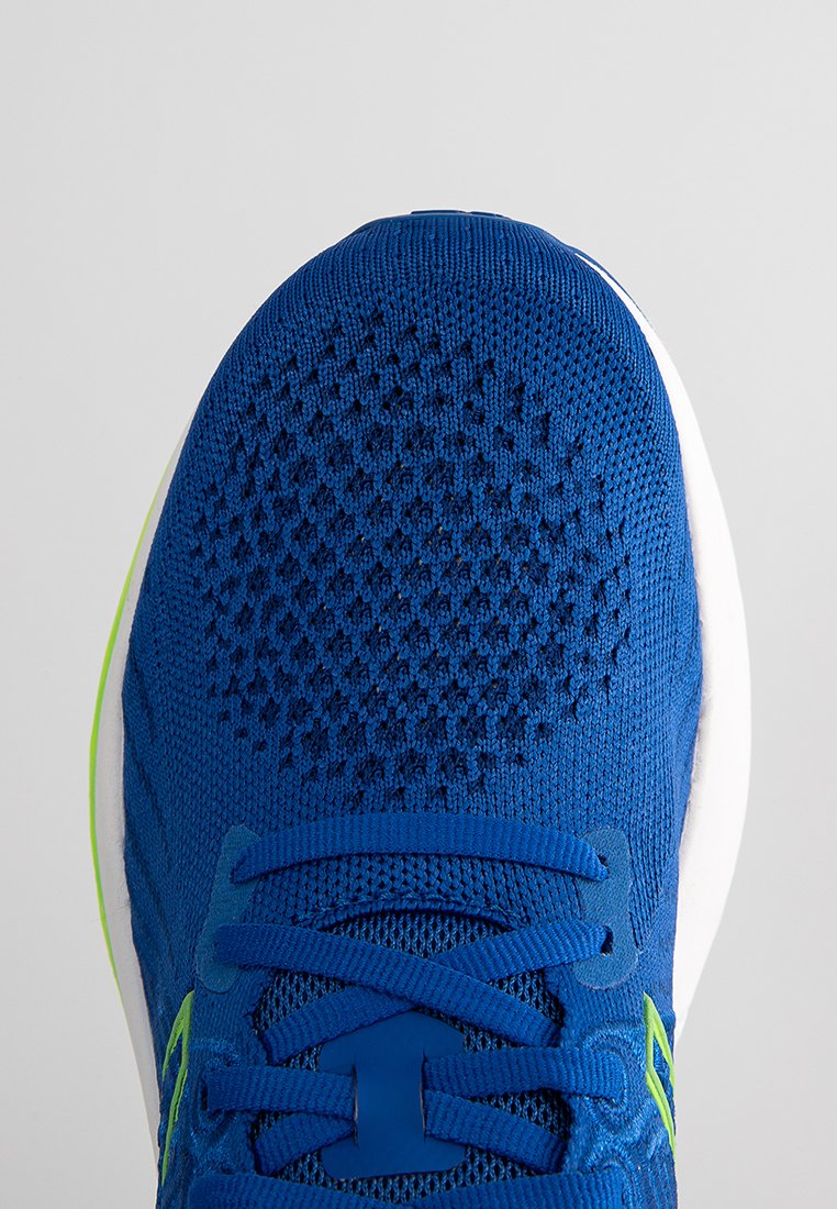 Zapatilla deportiva azul con parte superior de malla transpirable, puntera redondeada, superficie texturizada y suela blanca ligera y acolchada. Acentos verdes visibles.