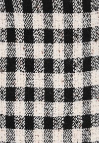 Fekete és krémszínű szőtt textilelem, amely kockás mintájú, váltakozó négyzetformákkal és változatos textúrákkal, hangsúlyozva a bolyhos szálakat.