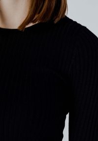Top lungo a maniche nere a costine, caratterizzato da un design aderente e un tessuto testurizzato, con scollatura tonda e spalle senza cuciture.