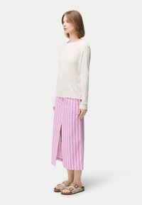 Vit texturerad långärmad skjorta kombinerad med en midjekjol med rosa ränder och en slits framtill, kompletterad med bruna slip-in sandaler.