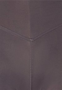 Nahaufnahme eines grauen Stoffs mit sichtbaren doppelten Nähten, die ein T-förmiges Muster bilden.