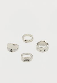 Quatre anneaux argentés brillants aux formes irrégulières et organiques disposés sur une surface blanche.