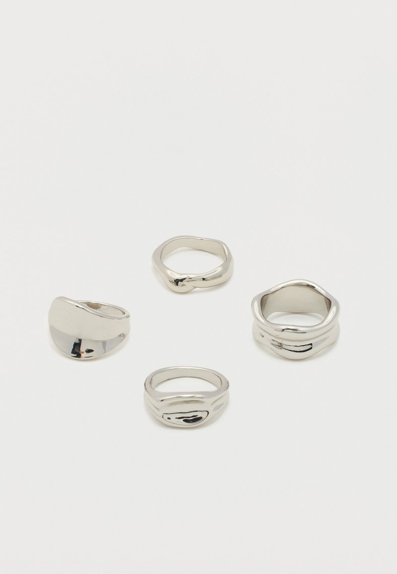Quatre anneaux argentés brillants aux formes irrégulières et organiques disposés sur une surface blanche.