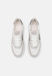Paire de baskets blanches et grises à lacets avec des accents en daim, vues de dessus sur un fond clair uni.